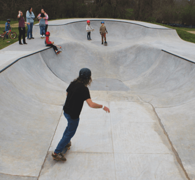A photo of an adult skater in the bowl at the skate park on a skate board surrounded by others
